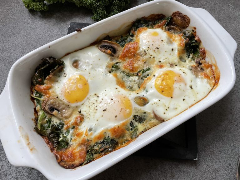 En ugnsbakad ägggryta i en vit skål med tre ägg, svamp, bladgrönsaker och smält ost på toppen -ett nyttigt val för dig som söker hälsosamma recept och funktionell mat.