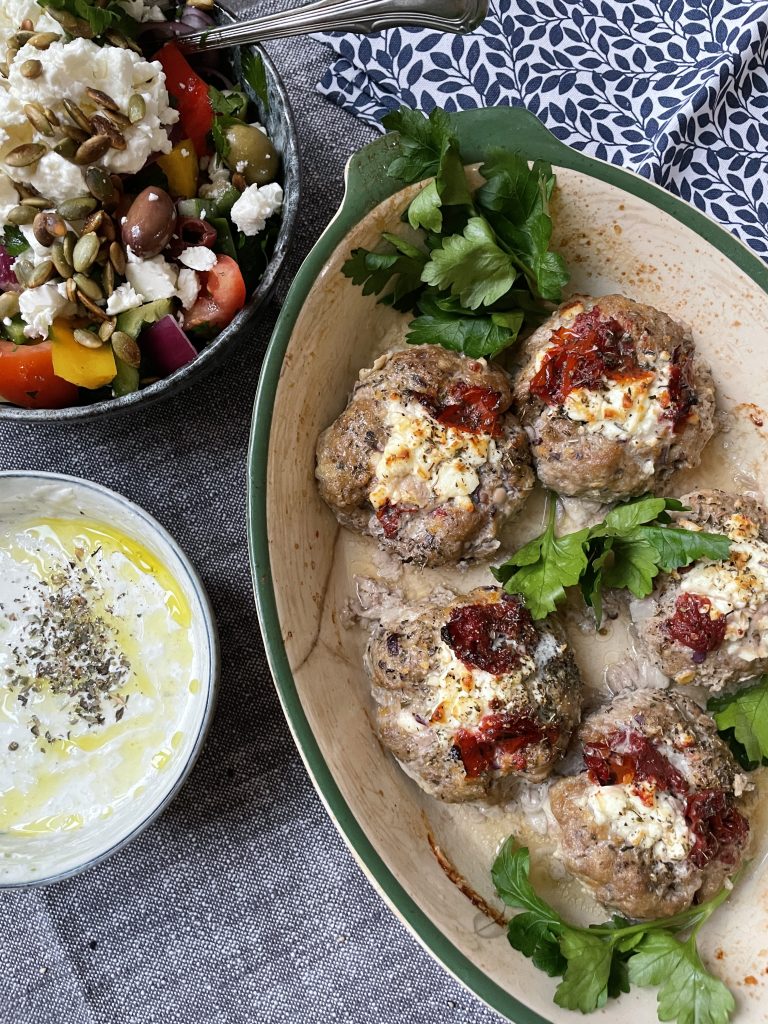 Bakade köttbullar toppade med ost och soltorkade tomater, serverade med en skål grekisk sallad och tzatziki - ett perfekt val för dem som söker hälsosamma recept och funktionella livsmedel.