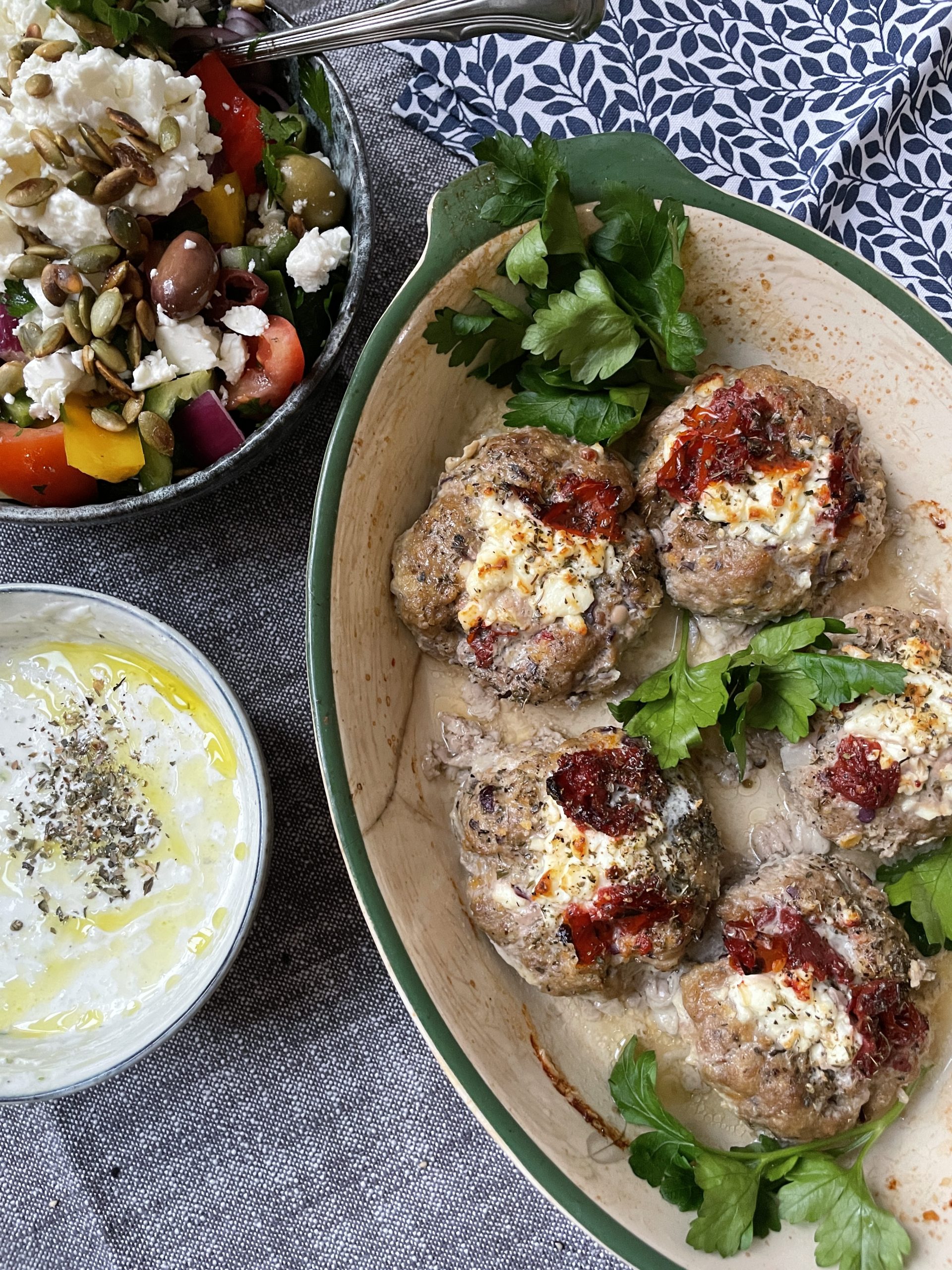 Bakade köttbullar toppade med ost och soltorkade tomater, serverade med en skål grekisk sallad och tzatziki - ett perfekt val för dem som söker hälsosamma recept och funktionella livsmedel.